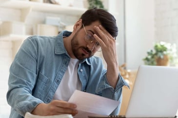 frustrated man looking at papers and computer